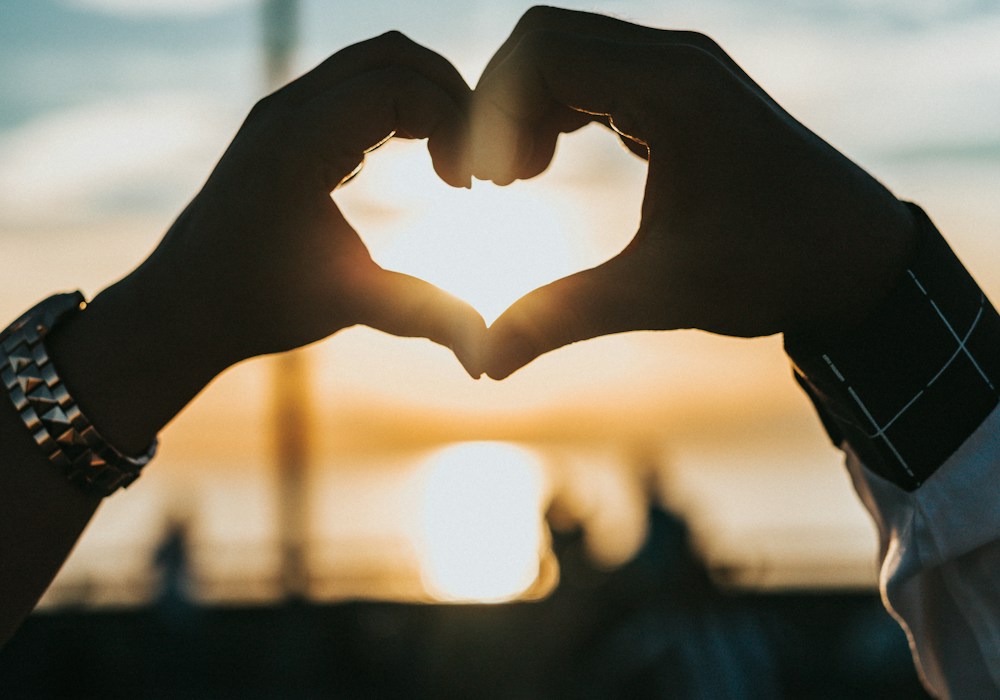 Two hands forming a heart at sunset — a quiet symbol of connection